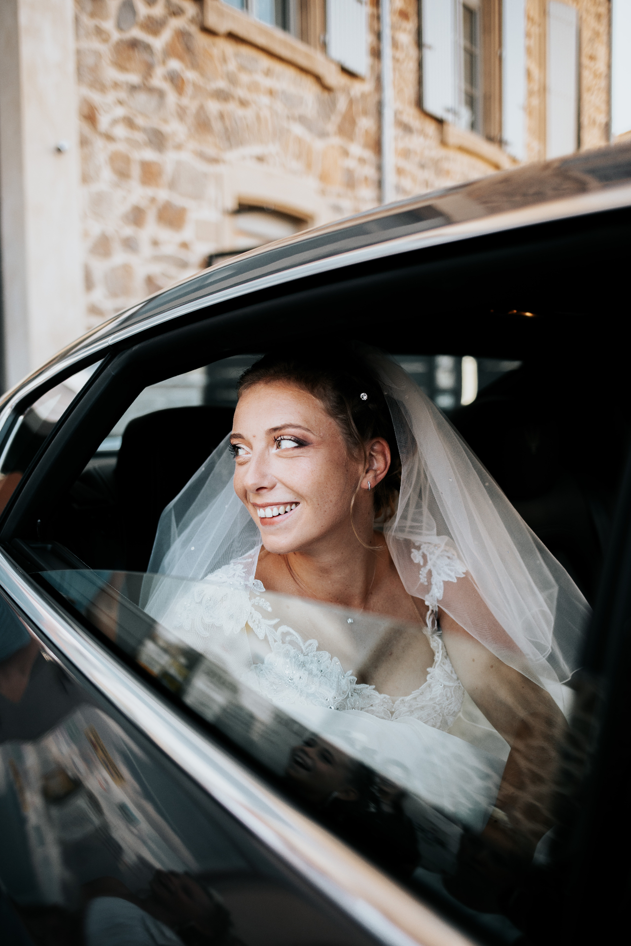 Mariée voilée souriante à la fenêtre de la voiture